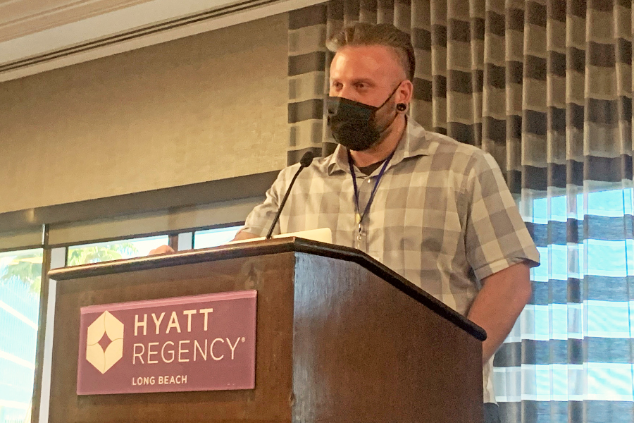 man wearing a black face mask speaks at a podium during a journalism awards convention at the hyatt regency long beach