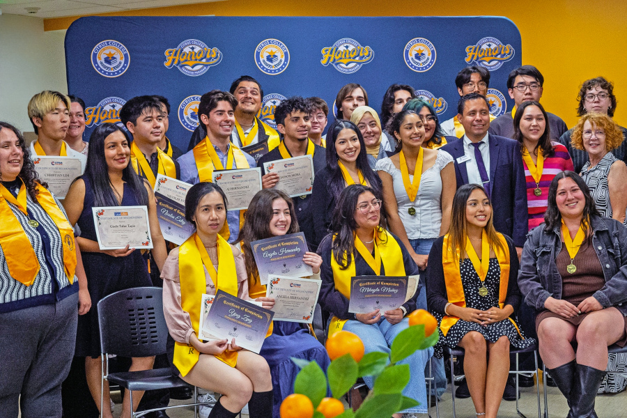 honors students wear medals and hold certificates during an end-of-year recognition celebration with faculty and staff nearby