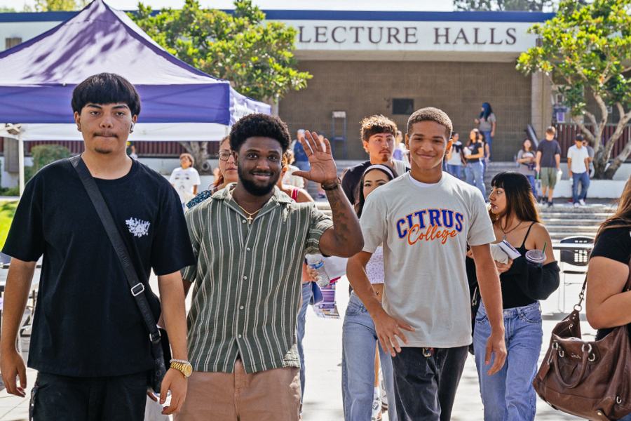 students walk through campus near lecture halls during an outdoor event, with one student waving and another wearing a citrus college shirt