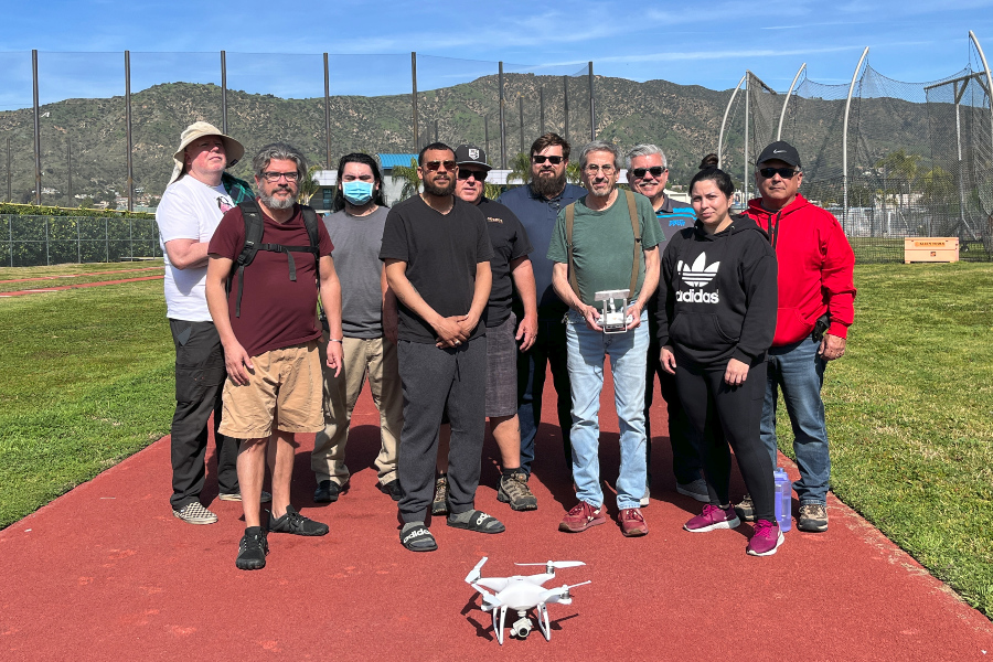 group of students and instructors posing with a drone on a campus athletic field