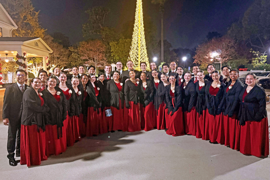 large choir group in red and black performance attire posing outdoors at night near holiday lights