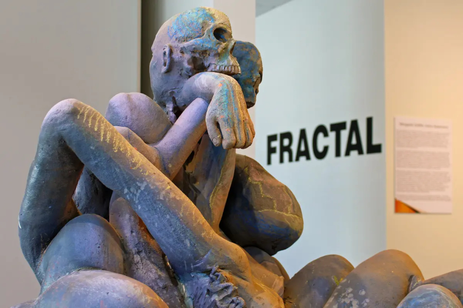 three dimensional sculpture of intertwined human figures with fractal exhibit sign in the background