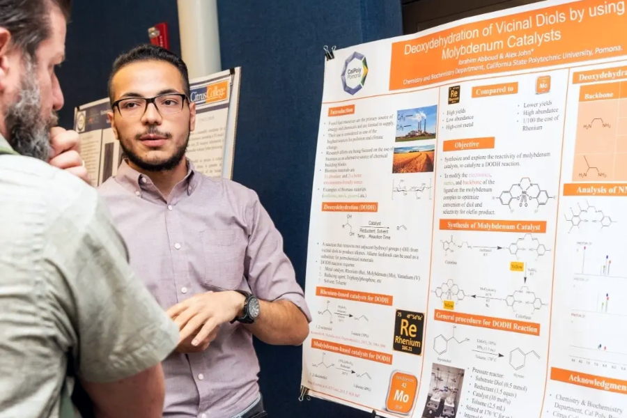 student Ibrahim Abboud student presents his research beside his scientific poster titled Deoxydehydration of Vicinal Diols by Using Molybdenum Catalysts, featuring chemical structures, diagrams, charts and research findings