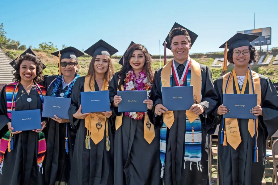six citrus college graduates in caps and gowns hold diploma covers while posing together outdoors at commencement
