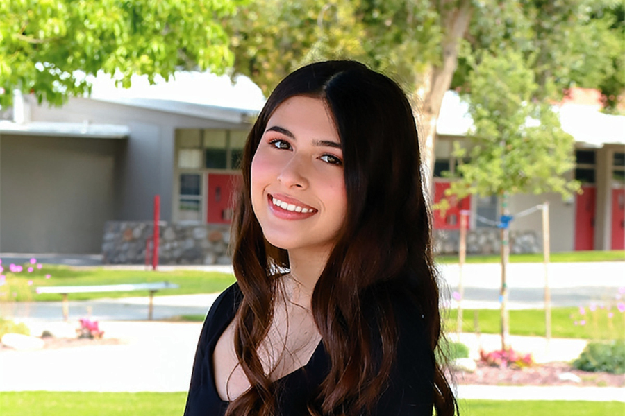 student smiles while seated outdoors a school campus
