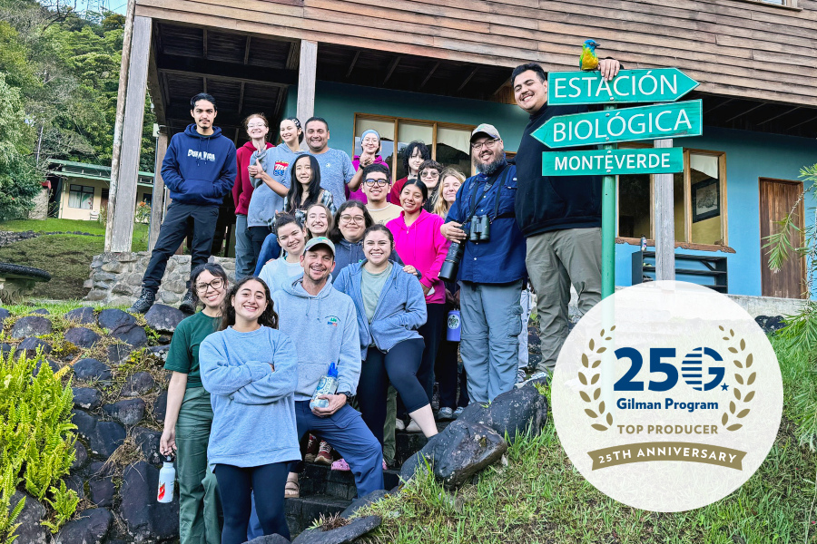 group of citrus college study abroad students and faculty standing outside a building at estación biológica monteverde in costa rica, gathered beside a green sign marking the biological station. gilman program 25th anniversary top producer badge appears in the lower corner