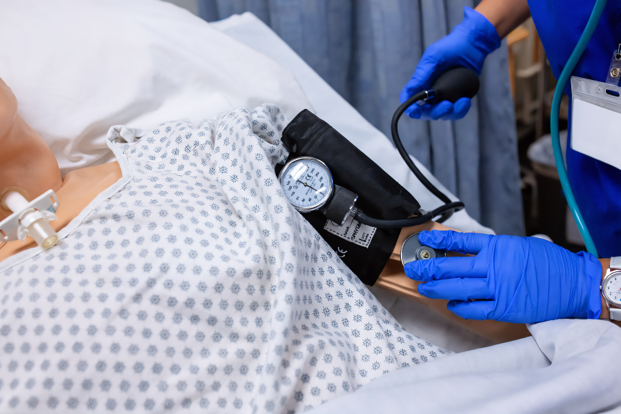 nursing student practices taking a patient's blood pressure and listening with a stethoscope on a medical simulation mannequin