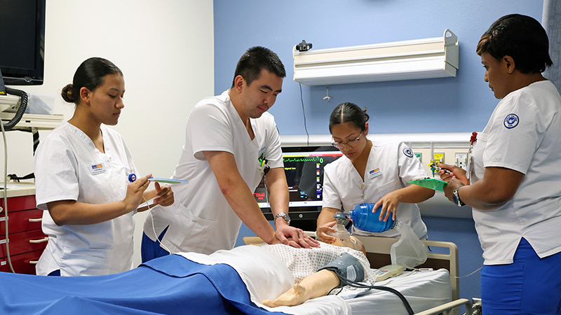 students in medical training uses a simulation mannequin to practice a clinical procedure while wearing gloves and a stethoscope in a lab setting