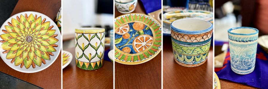 five hand-painted ceramic pieces with floral, leaf, citrus and scroll patterns are displayed side by side on a wooden table
