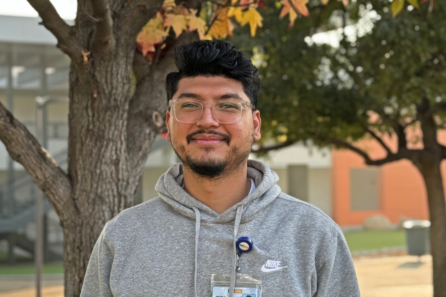 Jair Mejia stands outdoors on the Citrus College campus wearing glasses, a gray sweatshirt and a college identification badge
