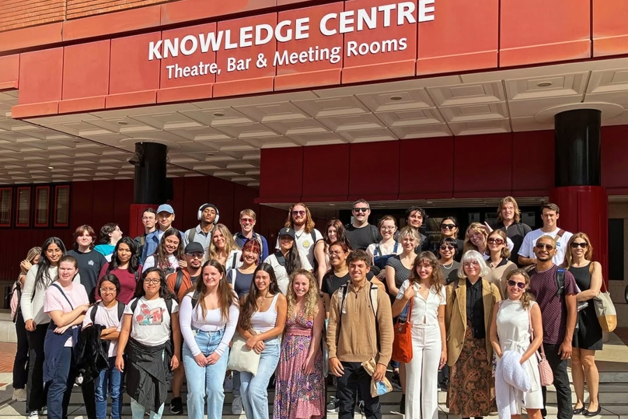 students pose on the steps outside the knowledge centre in london, with the entrance sign for the theatre, bar and meeting rooms displayed above them