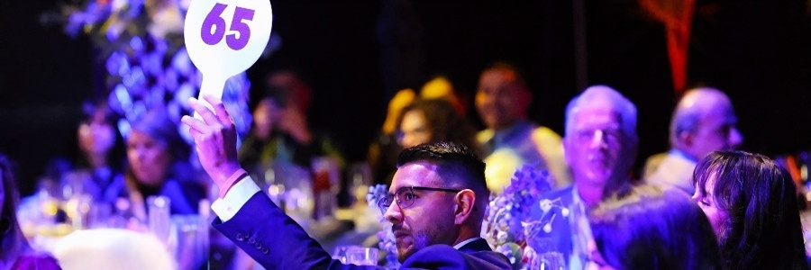 a gala guest raises a paddle marked 65 during a live auction as attendees watch from nearby tables