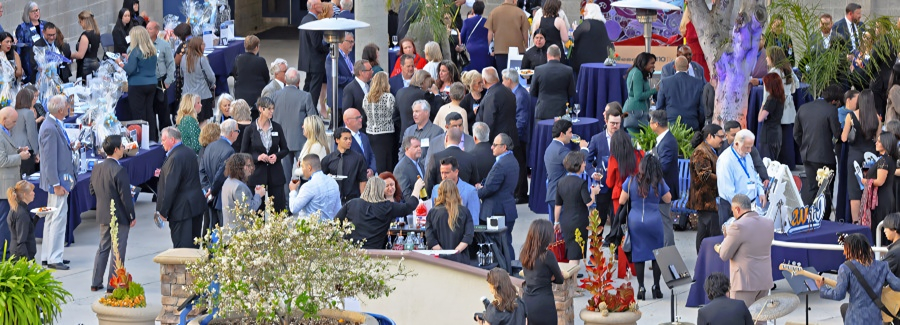 guests mingle at an outdoor anniversary gala reception with decorated cocktail tables, floral displays, food stations and live music