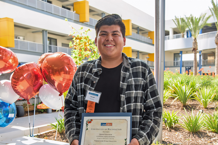 citrus college scholarship recipient holds a certificate beside orange, white and blue balloons during the foundation's scholarship reception