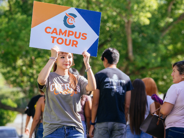 student tour guide holding a campus tour sign while leading a group along an outdoor campus walkway