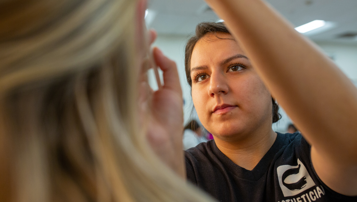 student in esthetician training carefully applying a client's makeup in a classroom setting, focused on hands-on learning and precision technique