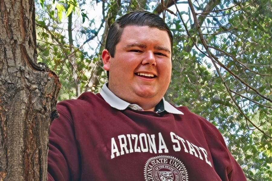 student wearing an arizona state university sweatshirt poses outdoors near a tree