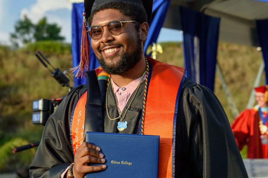 student graduate smiles while holding a citrus college diploma cover during commencement