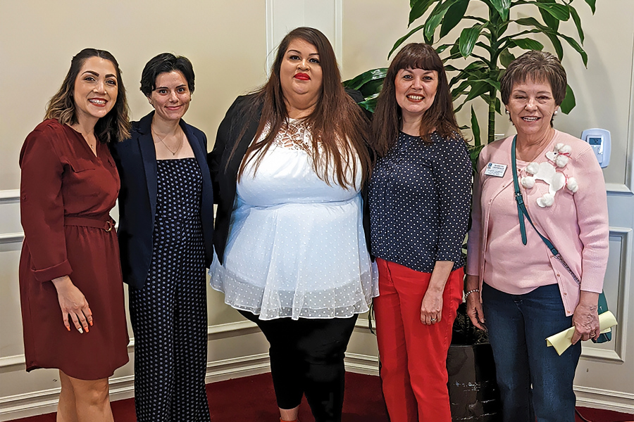 five women pose together at a soroptimist scholarship ceremony indoors with a large plant in the background