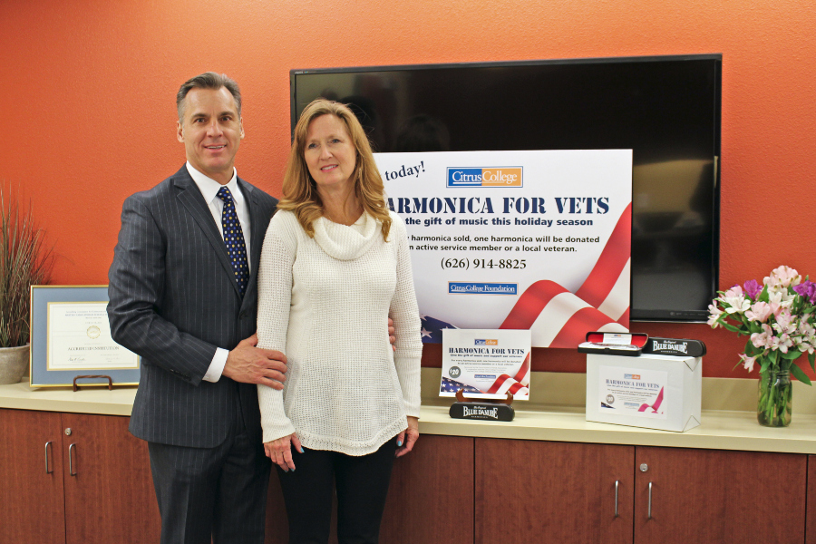 a man and woman stand beside harmonica for vets promotional materials and boxed harmonicas at citrus college