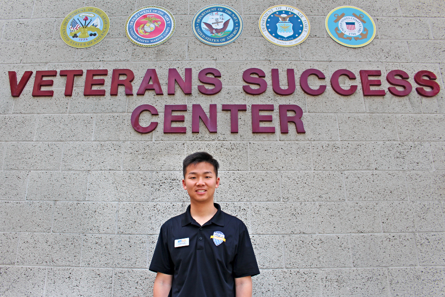 Jixiang Bian stands outside the Veterans Success Center beneath military branch emblems