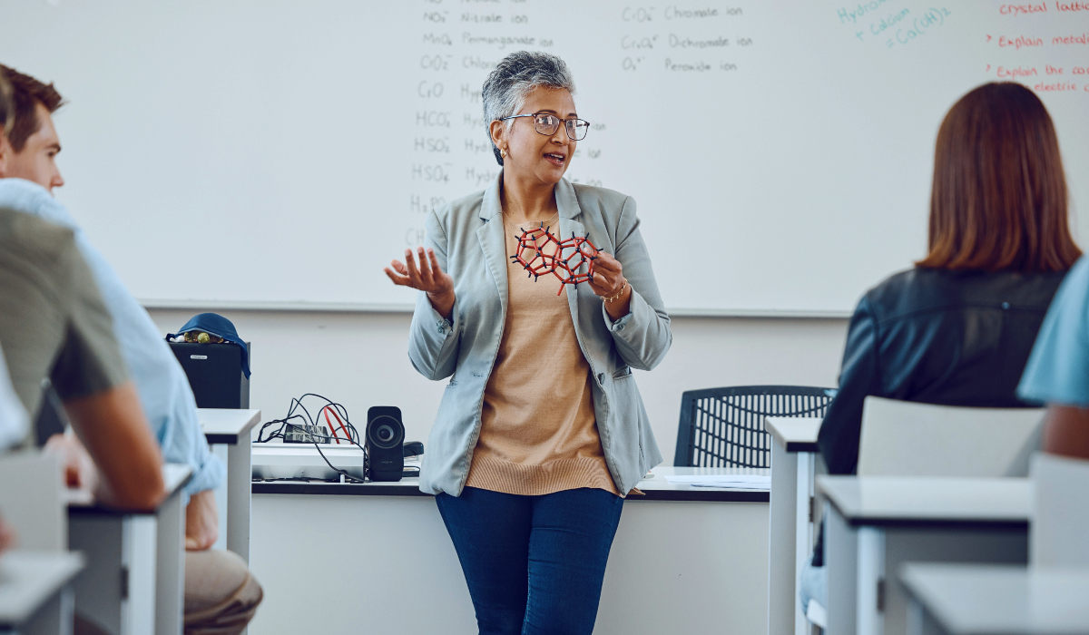 instructor holds a molecular model while teaching students in a chemistry classroom