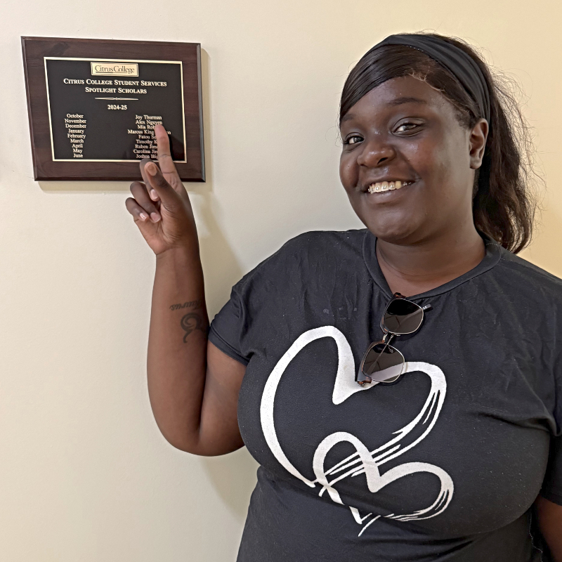 Joy Thurman pointing to her name engraved on a student services Spotlight Scholars plaque