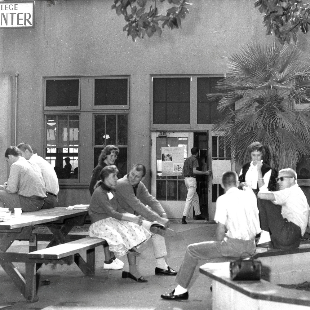 black-and-white archival photo from 1968 of students socializing at picnic tables and benches outside the student center building